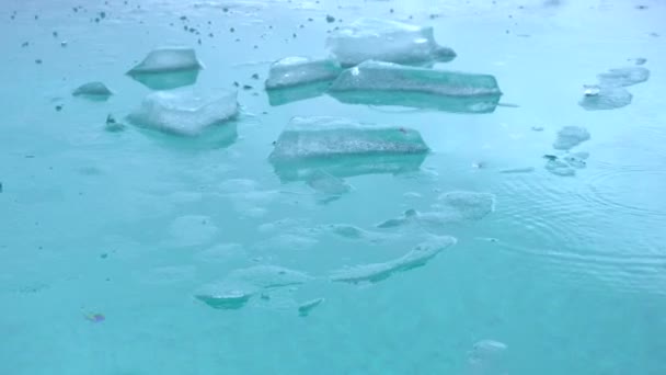 Gelo na piscina. Gotas de chuva na superfície da água, com blocos de gelo. Um pequeno termômetro de peixe amarelo flutua na piscina entre as geleiras . — Vídeo de Stock