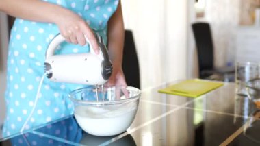 Kadın şef yumurtanın beyazını cam bir kabın içinde karıştırıcı ile karıştırıyor..