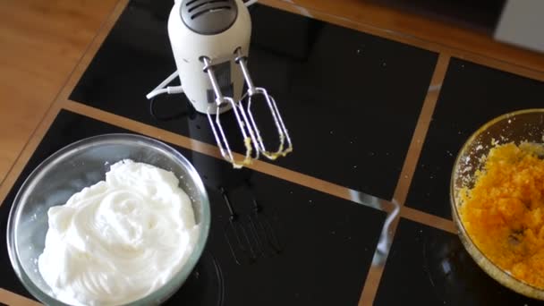 På det svarta bordet finns en elektrisk mixer, en glasskål med vispade äggvitor och en skål med äggula blandat med socker. Beredning av bakverk. — Stockvideo