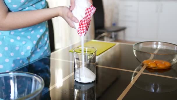 Uma chef feminina derrama açúcar branco de um pacote em um copo de medição de vidro em uma mesa em uma cozinha doméstica . — Vídeo de Stock