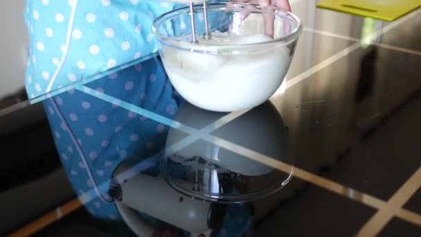 Kobieta szef kuchni miesza białko z mieszalnikiem w szklanej przezroczystej misce do stanu białej przewiewnej pianki. — Wideo stockowe