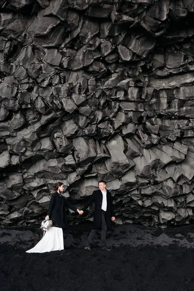 Mariage Destination Islande. Couple de mariage sous un rocher de pierres de basalte. Mariée et marié sur la plage noire de Vik . — Photo