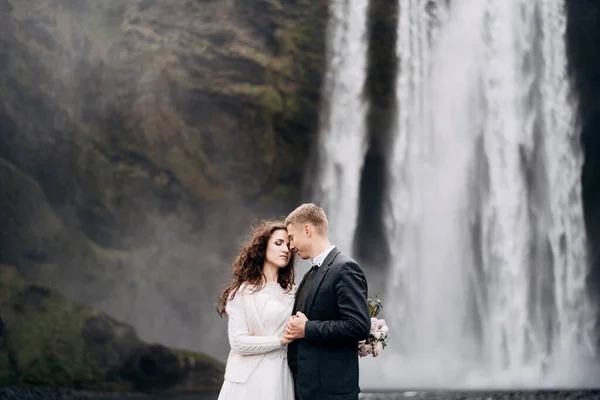 Couple de mariage près de la cascade de Skogafoss. Mariage Destination Islande. Les mariés se tiennent la main et touchent le front . — Photo