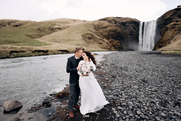 Mariage Destination Islande. Couple de mariage près de la cascade de Skogafoss. Les mariés s'étreignent près de la rivière . — Photo