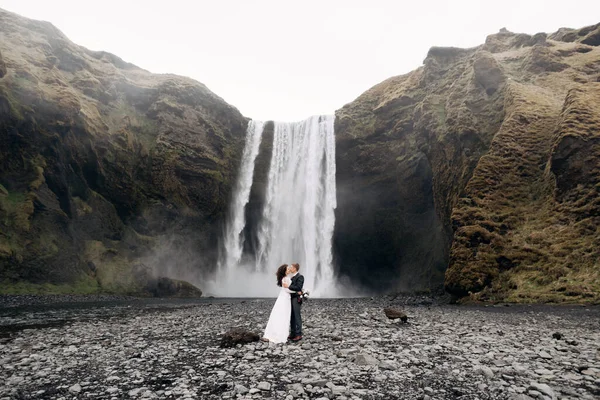 Skogafoss 폭포 근처의 결혼식 부부. 아이슬란드의 결혼을 기념 한다. 신랑은 신부에게 입을 맞추고. — 스톡 사진