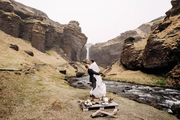 Kvernufoss 폭포 근처에서 열리는 아이슬란드 결혼식입니다. 산기슭에서 결혼 한 부부가. 신랑은 모직 담요를 손에 끼고 신부를 입고 있다. — 스톡 사진