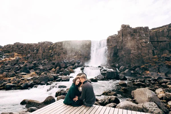 Un homme et une fille sont assis embrassant sur un pont près de la cascade d'Ehsaraurfoss, rivière Ehsarau, parc national, Thingvedlir, la région de Sudurland, Islande . — Photo