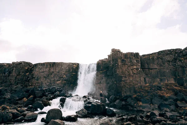 Een man in een zwarte gebreide trui staat op rotsen bij Ehsaraurfoss Falls, Ehsarau River, National Park, Tingvedlir, Syudurland Region, IJsland. — Stockfoto