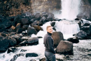 Ehsaraurfoss Şelaleleri, Ehsarau Nehri, Ulusal Park, Tingvedlir, Syudurland Bölgesi, İzlanda yakınlarındaki kayalıklarda siyah örülü bir süveter giyen bir adam duruyor..