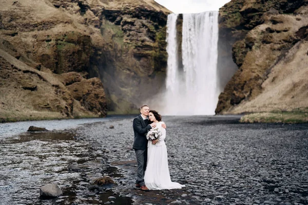 Casamento destino Islândia. Casamento casal perto Skogafoss cachoeira. A noiva e o noivo abraçam-se perto do rio. . — Fotografia de Stock