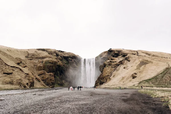 Cascade de Skogafoss au sud de l'Islande, sur l'anneau doré. Les visiteurs sont venus voir la cascade, les touristes marchent au pied de la montagne . — Photo