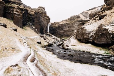 İzlanda 'nın güneyindeki Kvernufoss şelalesine giden yol, Altın Halka üzerinde. Dağ nehri yosun ve sarı otlarla kaplı bir vadide, karla kaplanmış..