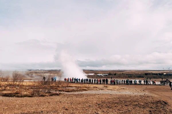 Tourists look at the eruption of a geyser. Geyser Valley in southwest of Iceland. The famous tourist attraction Geysir. Geothermal zone Haukadalur. Strokkur geyser on the slopes of Laugarfjall hill.