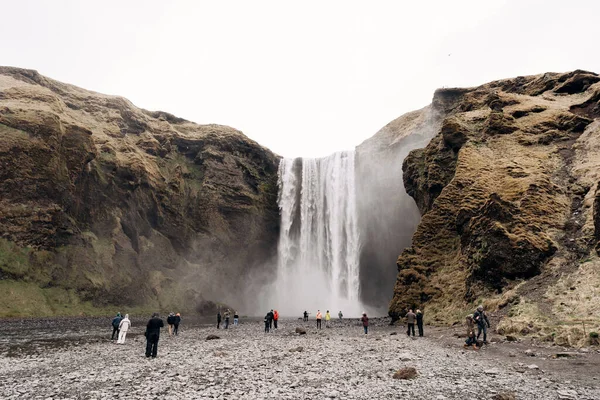 Skogafoss vízesés Izland déli részén, az aranygyűrűn. Látogatók jöttek megnézni a vízesést, turisták sétálnak a hegy lábánál.. — Stock Fotó