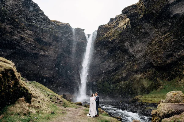 Tujuan pernikahan Islandia, dekat air terjun Kvernufoss. Pasangan pengantin berdiri di dekat air terjun. Pengantin pria memeluk pengantin wanita. — Stok Foto