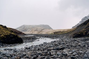 İzlanda 'daki Rocky sığ dağ nehri, dağların arka planına doğru akar..