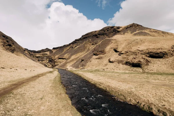 Швидка гірська річка тече серед жовтого сухої трави на тлі маленьких гір в Ісландії проти блакитного неба з білими хмарами.. — стокове фото