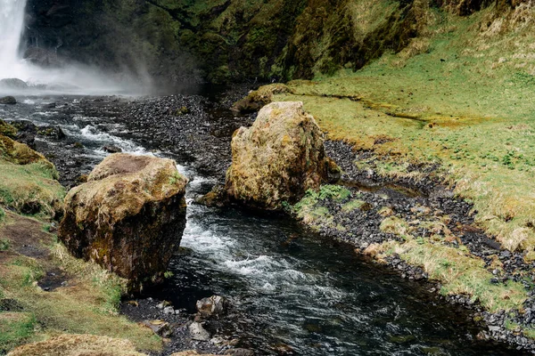 A small mountain river flows between two boulders in the mhu, from the waterfall Kvernufoss in Iceland. — Stock Photo, Image