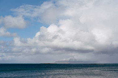 İzlanda 'nın Atlantik kıyısında karla kaplı bir dağ. Diğer taraftan bak, ya da denizden. Bulutlu hava, yoğun bulutlar.