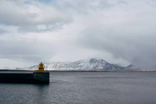 Fyrtorn på havsbrygga i Reykjavik Island. Fyrens gula ljusa torn vid havets strand. Hamnnavigeringskoncept. Sjötransport och navigering. Seascape och skyline med ljusa fyr. — Stockfoto