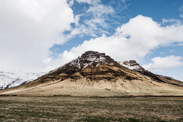 Monte rochoso de pico coberto de neve coberto com grama seca amarela na Islândia . — Fotografia de Stock