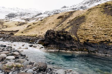 Dağ nehri dağın eteğinde karla kaplı bir tepesi var. Mayıs ayında İzlanda 'da dağlarda sarı kuru otlar.