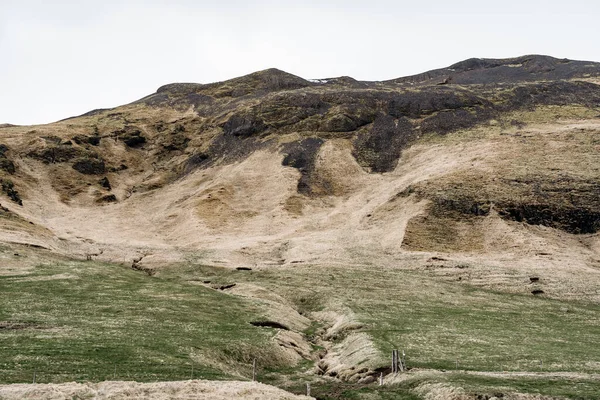 Une prairie verte avec un sillon pour la collecte de l'eau de montagne, avec de l'herbe verte. Dans le contexte d'une colline avec herbe jaune en Islande . — Photo