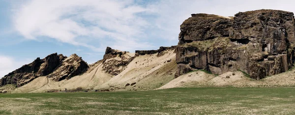 Un prado verde, un campo para pastorear ganado con hierba, sobre el telón de fondo de montañas rocosas y cielo azul con nubes blancas en Islandia . — Foto de Stock