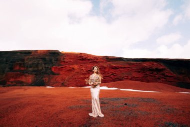 Altın bir gelinlik içinde bir gelin modeli portresi, sarı-kırmızı bir taş ocağında, İzlanda 'da bir volkanın kraterinde, Altın Çember' de. Vazodaki altın dallar ve enstrümanlar..