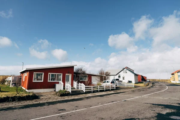 Un condominio rosso con finestre bianche e una recinzione, sulla strada di una zona residenziale in cui vivono gli islandesi. Strada asfaltata in zona notte. Cielo blu con nuvole bianche . — Foto Stock