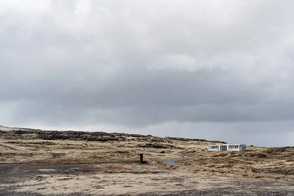 Gul torr gräs till horisonten, en väg som går i fjärran, ett ensamt hus som står på en kulle på Island. — Stockfoto