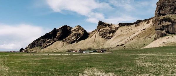 Casas residenciais e instalações de produção de empresas agrícolas, no sopé da montanha na Islândia. Prado verde para pastagem . — Fotografia de Stock