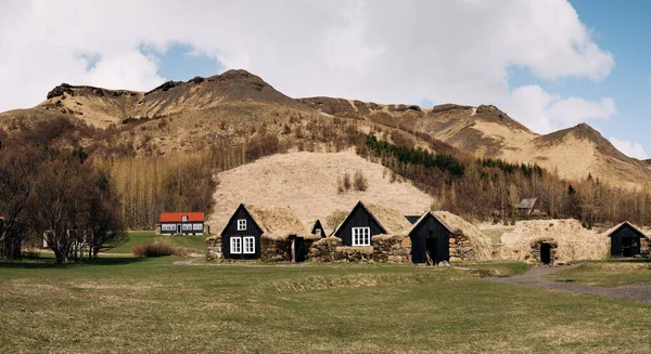 Ősi fekete faházak burzsoáziával a tetőn, az erdő és a hegyek hátterében Izlandon. — Stock Fotó
