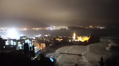 Karadağ 'ın eski Budva kenti yakınlarındaki sahilde fırtına dalgaları var. Gece şehrinin ışığı.
