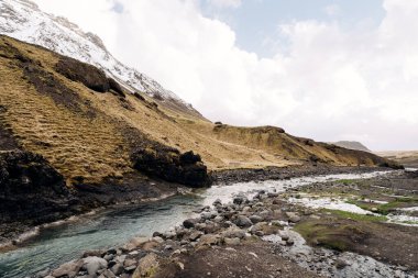 Mavi gök mavisi suyu ile sığ bir dağ nehri dağların zeminine, dağların tepelerine ve karla kaplı tepelere akar..