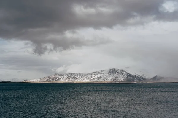 İzlanda 'nın Atlantik kıyısında karla kaplı bir dağ. Diğer taraftan bak, ya da denizden. Bulutlu hava, yoğun bulutlar. — Stok fotoğraf