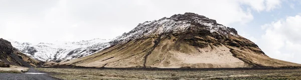 Panorama hory je pokryto žlutou suchou trávou a omomomou na Islandu. Zasněžený vrchol hory proti mrakům na obloze. — Stock fotografie