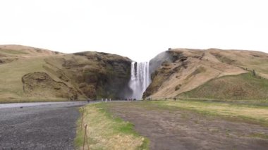 Skogafoss Şelalesi İzlanda 'nın güneyinde, altın yüzüğün üzerinde. Şelaleyi görmeye gelen ziyaretçiler, dağların eteklerinde yürüyen turistler..