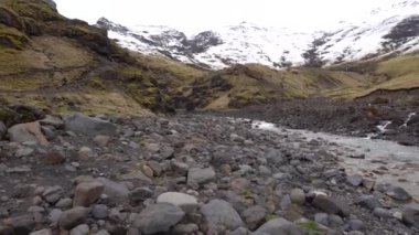 Küçük sığ dağ nehri, karla kaplı dağlardan vadiye akıyor, şelale çağlayanı üzerinde. Karla kaplı dağın tepesi ve ayağı sarı kuru çimlerde.. 
