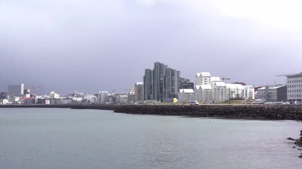 Moderne hoogbouw met meerdere verdiepingen aan de waterkant in Reykjavik, de hoofdstad van IJsland. De kust van de Atlantische Oceaan, het stille water is rustig. Bewolkte lucht, een sneeuwstorm nadert.. — Stockvideo