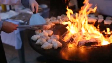 Balık, tenceresi ve ortasında ateş bulunan yuvarlak çelik bir ızgarada hazırlanıyor. Şef, forseps ve spatulayla balığı çevirir..