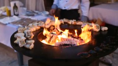 Balık, tenceresi ve ortasında ateş bulunan yuvarlak çelik bir ızgarada hazırlanıyor. Aşçı eliyle etin sıcaklığını ölçer, fileto cımbızı ters çevirir..