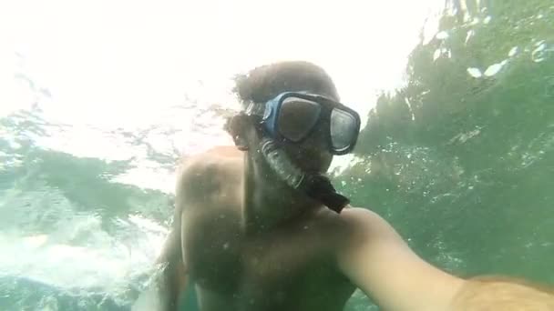 El tipo se sumerge en el agua. Un primer plano de la cara de los buceadores, Un joven nada bajo el agua en el mar, En ella hay vasos para bucear, Los rayos del sol rompen el agua . — Vídeos de Stock