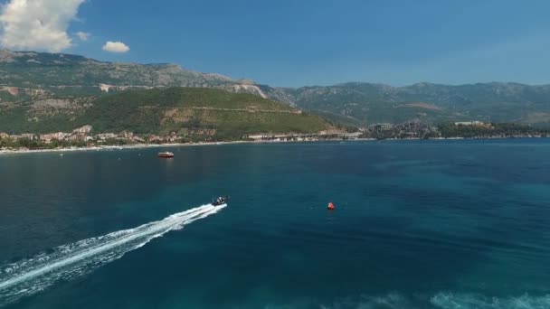 En snabb motorbåt rusar genom det blå havsvattnet, nära kusten i Budva, Montenegro. — Stockvideo