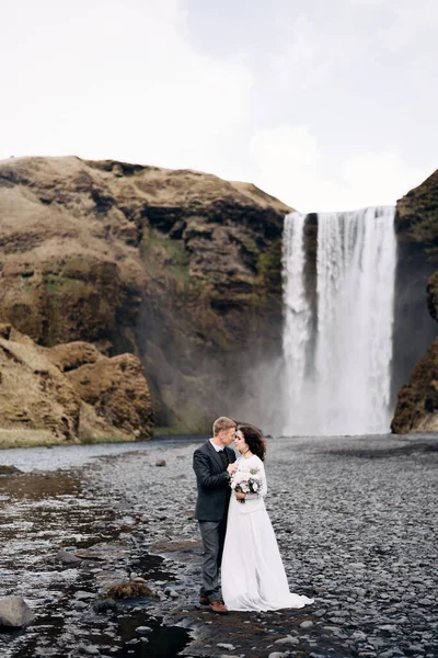 Tujuan pernikahan Islandia. Pasangan pernikahan dekat air terjun Skogafoss. Pengantin wanita dan pengantin pria berpelukan di dekat sungai. — Stok Foto