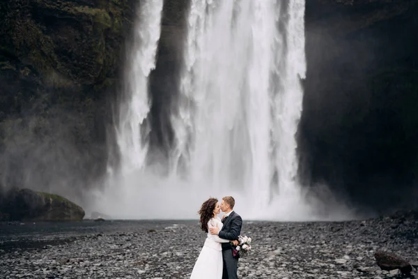 Pasangan pernikahan dekat air terjun Skogafoss. Tujuan pernikahan Islandia. Pengantin pria mencium pengantin wanita. — Stok Foto