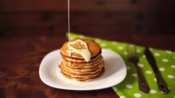 Kondenserad mjölk hälls på en bunt pannkakor. — Stockvideo