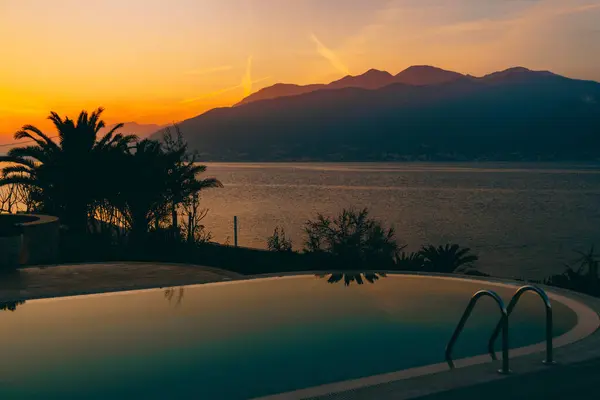 Le coucher de soleil ardent se reflète dans la piscine, sur fond de mer, de montagnes et de palmiers . — Photo