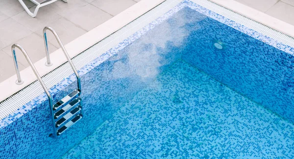 A chrome staircase with railings in a pool with blue mosaic.