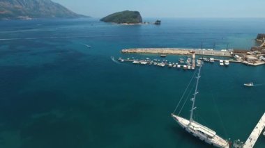 Karadağ 'ın eski Budva kenti yakınlarındaki bir rıhtıma demirlemiş büyük bir yelkenli yat. Adriyatik Denizi 'nin mavi masmavi suyu. Aziz Niklas Adası ve Budvan Riviera kıyıları.